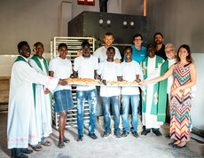 Die Bäcker der neuen Bäckerei in Uganda stehen gemeinsam mit Förder*innen dem jetzigen Bischof von Kärnten Josef Marketz, sowie Bereichsleiterin der Caritas Kärnten für die Auslandshilfe Alexandra Blattnig Rull vor den großen Backöfen und einem Blech voll frisch gebackenen Brot.