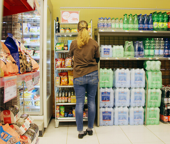 Eine Mitarbeiterin mit langen blonden Haaren steht vor den Getränke-Regalen des SPAR Supermarktes Perspektive Handel in Villach und räumt diese ein.