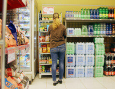 Eine Mitarbeiterin mit langen blonden Haaren steht vor den Getränke-Regalen des SPAR Supermarktes Perspektive Handel in Villach und räumt diese ein.