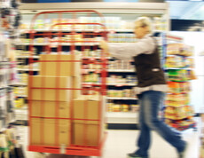 Eine SPAR Supermarkt Perspektive Handel-Mitarbeiterin fährt mit einem Rollwagen und neuen Waren durch den Gang des Supermarktes.