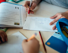 Man sieht die Hände eines Lernhelfers, der einem Schüler gerade eine Aufgabe Schritt für Schritt anhand einer Rechnung auf einem Blatt erklärt.