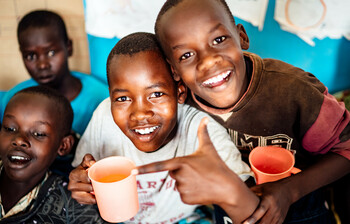 Eine Gruppe an Kindern in Afrika mit bunten Trinkbechern in der Hand lächeln.