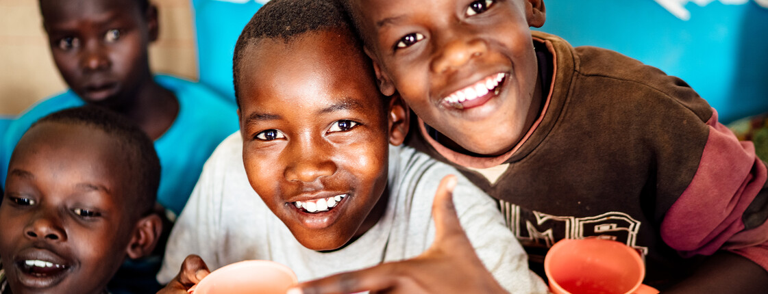 Eine Gruppe an Kindern in Afrika mit bunten Trinkbechern in der Hand lächeln.