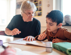 Ein Mann sitzt mit einem Jungen am Tisch auf dem auch Heft, Spitzer und Federpenal liegen. Er erklärt dem Jungen gerade eine Aufgabe. Der Junge sieht konzentriert in das Heft.