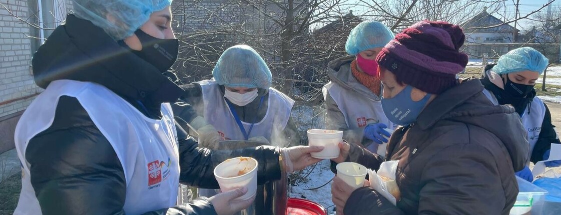 Man sieht Frauen mit Caritas-Kleidung beim Austeilen von Suppe an eine Frau