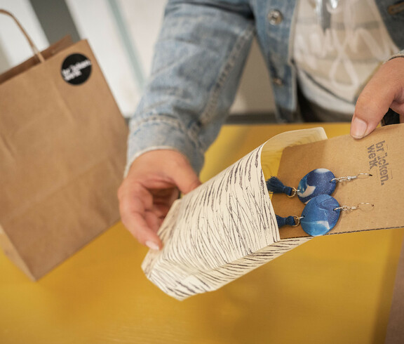 Eine Verkäuferin legt gerade einer Kundin ein selbst geknüpftes Armband an.