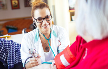 Eine Diplomierte Gesundheits- und Krankenpflgerin misst den Blutdruck bei einer älteren Dame.