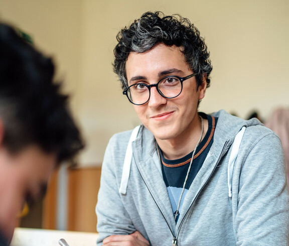 Ein freiwilliger Lernhelfer lächelt einen Schüler des Lerncafés, der gerade seine Aufgaben macht, an.