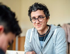 Ein freiwilliger Lernhelfer lächelt einen Schüler des Lerncafés, der gerade seine Aufgaben macht, an.