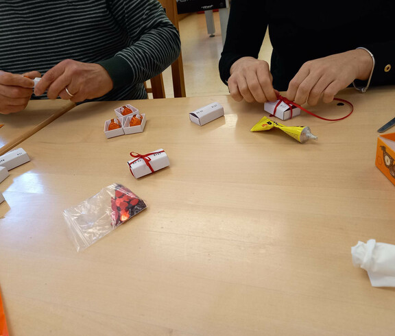 Menschen aus unserem Projekte rollen Sprüche auf Papier zusammen und verpacken diese mit einer Schleife.