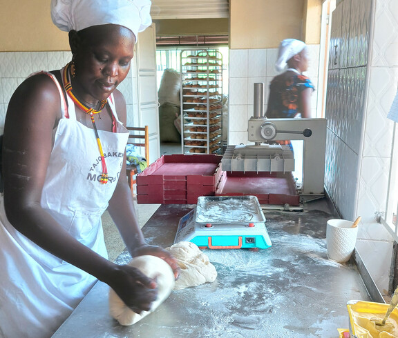 Eine Mitarbeiterin der Bäckerei knetet den Brotteig auf der Arbeitsfläche.