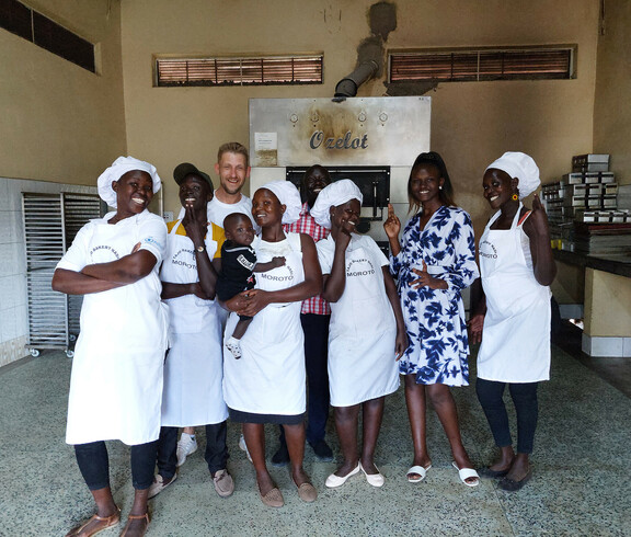 Das Team der neuen Bäckerei in Moroto steht stolz vor dem Ofen der Bäckerei und lächelt in die Kamera.