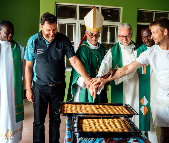 Der jetzige Bischof von Kärnten Josef Marketz und ein Bischof aus Uganda schneiden mit Projektförder*innen den ersten Kuchen der Bäckerei an.