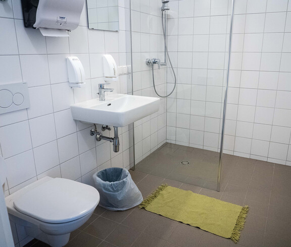 Die Sanitäranlagen der Notschlafstelle mit WC, Waschbecken und Spiegel sowie Dusche.