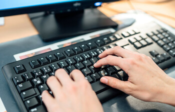 Frauenhände tippen etwas auf einer Computer-Tastatur ein.